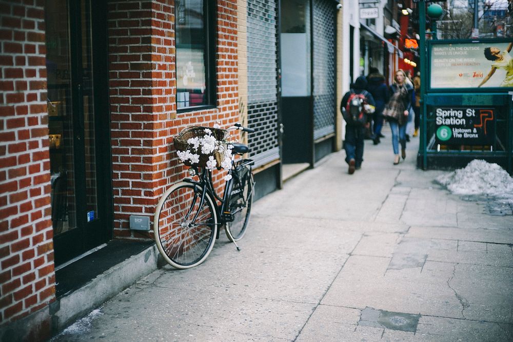 Bike with flowers and basket leaning against brick wall on sidewalk, Spring St. Original public domain image from Wikimedia…