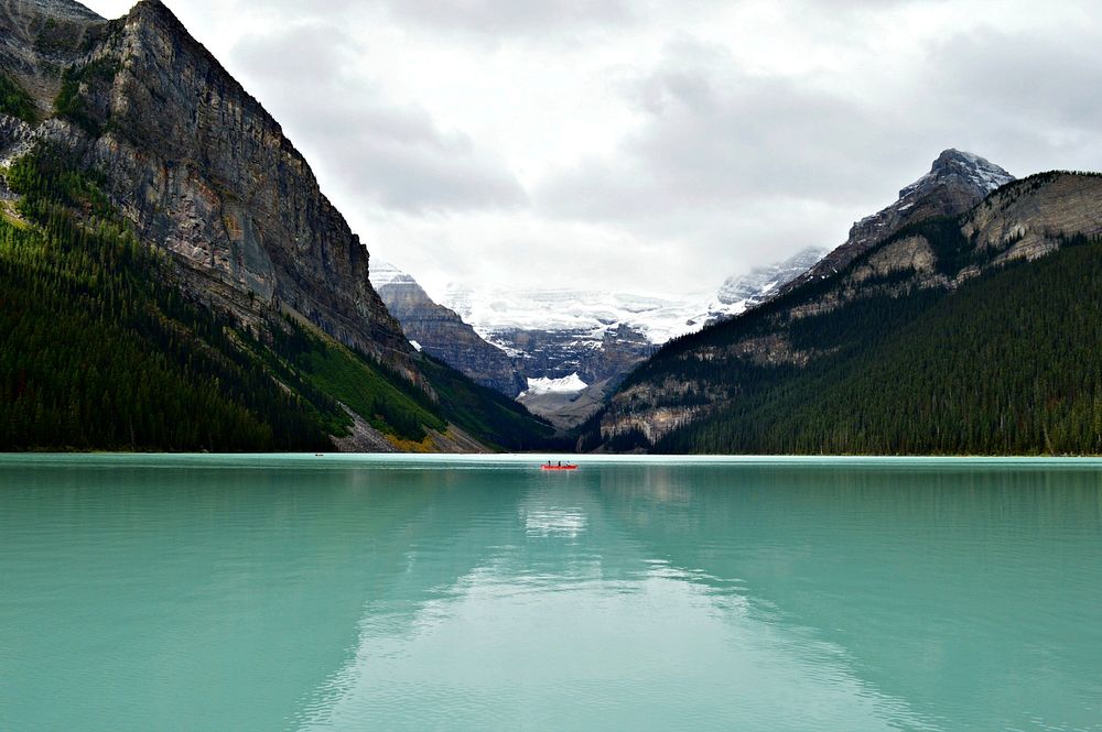 A red boat on the turquoise surface of Lake Louise surrounded by jagged mountains. Original public domain image from…