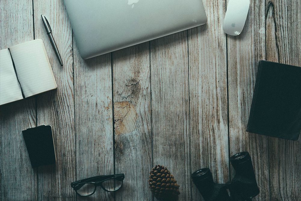 An unplugged typewriter on an office woodwork table holding a pinecone, glass and a writer’s book. Original public domain…