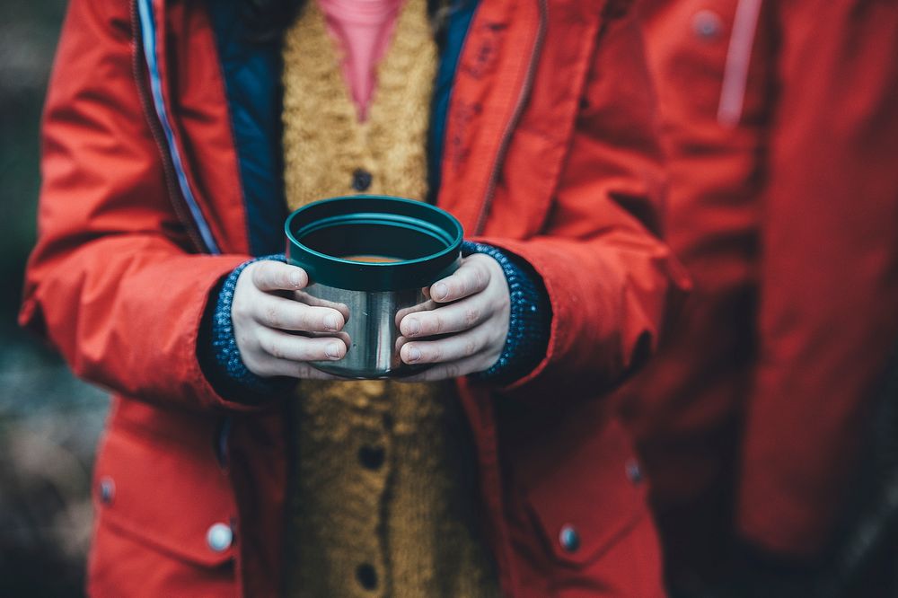 Child wearing raincoat, standing in the cold and holding cup of soup in New Forest District. Original public domain image…