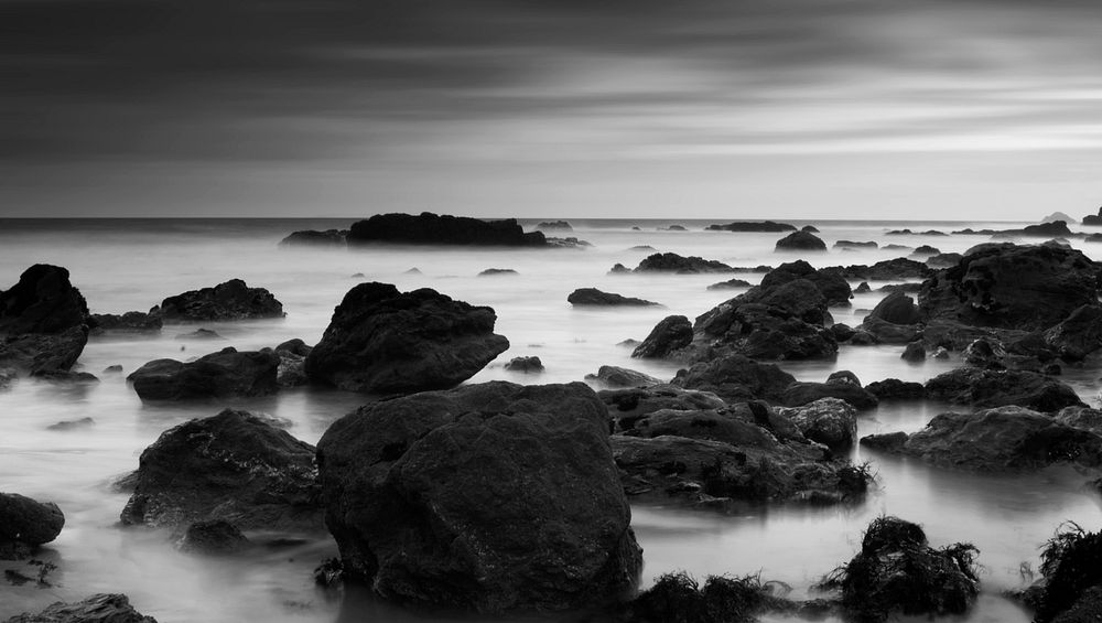 A black and white photo of rocks protruding from the ocean along the coast. Original public domain image from Wikimedia…