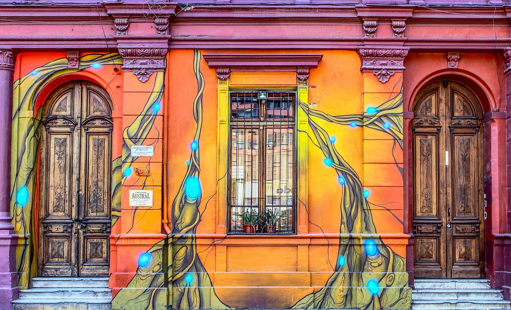 Colorful sunburst wall art on building wall with windows and wooden doors, Santiago. Original public domain image from…