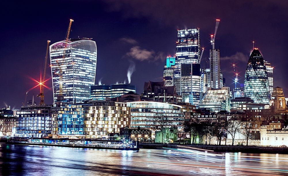 A cityscape background featuring well lit buildings and skyscrapers at night in London. Original public domain image from…