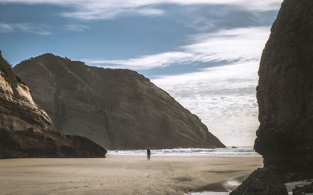 Person on a sand Wharariki Beach surrounded by tall cliffs. Original public domain image from Wikimedia Commons
