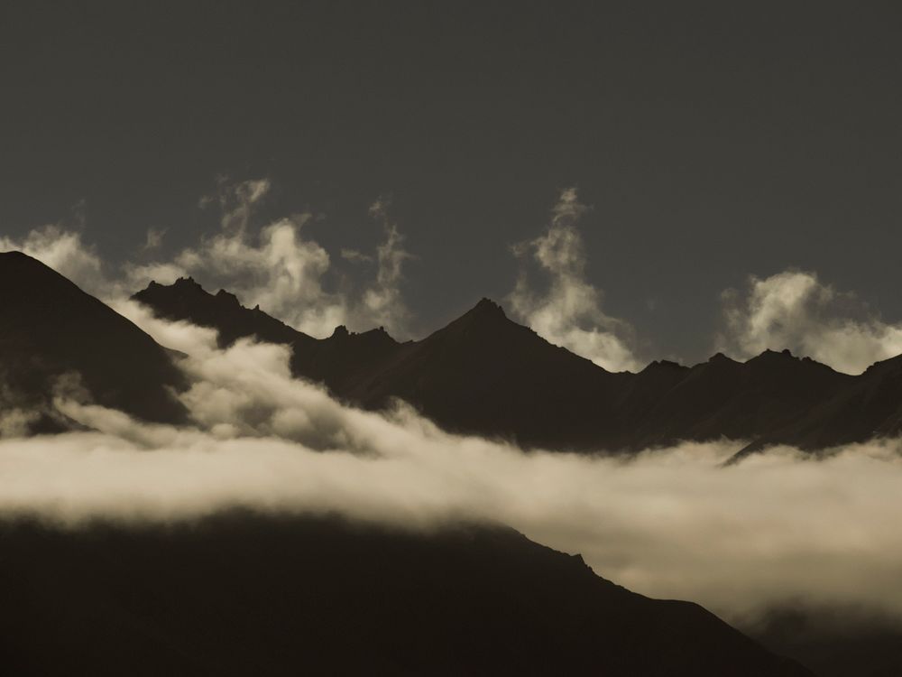 Silhouettes of sharp mountain peaks enveloped in white clouds near Lake Wanaka. Original public domain image from Wikimedia…