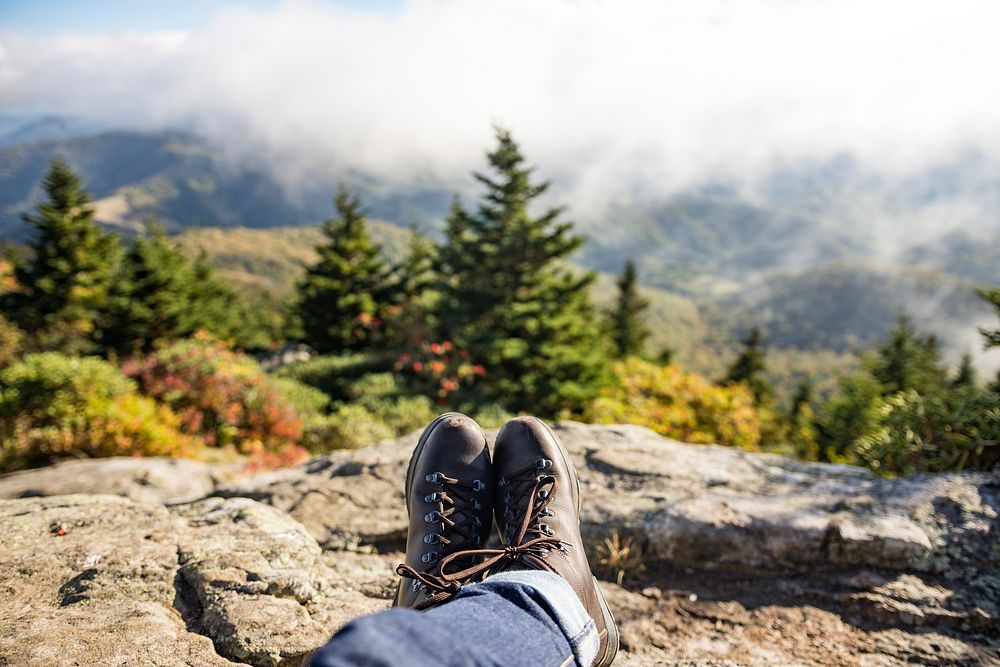 A person wearing hiking boots and jeans resting on a rock looking out into the fog covered mountains. Original public domain…