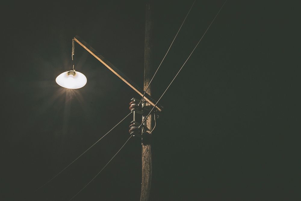 Single street lamp lit up by a power line at night. Original public domain image from Wikimedia Commons