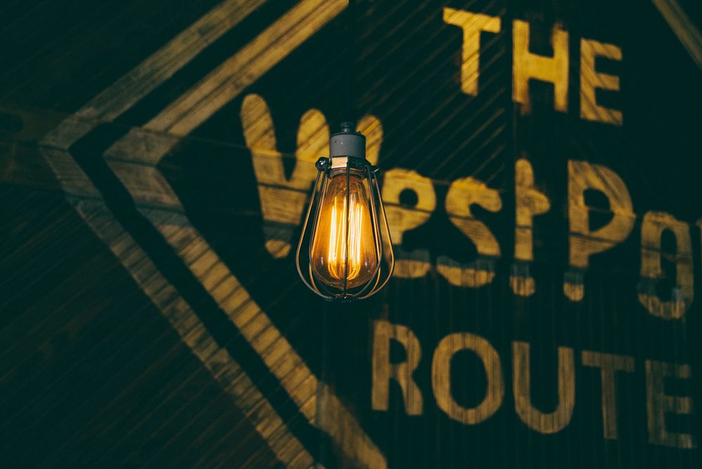 An incandescent light bulb near a sign on a wooden wall. Original public domain image from Wikimedia Commons