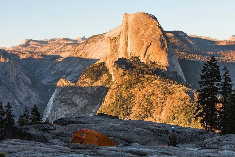 A hiker crouching near a tent during golden hours in Yosemite Valley. Original public domain image from Wikimedia Commons