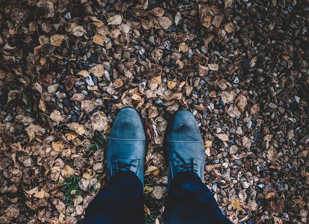 Looking down at a pair of blue boots in a pile of leaves on the floor in the autumn.. Original public domain image from…