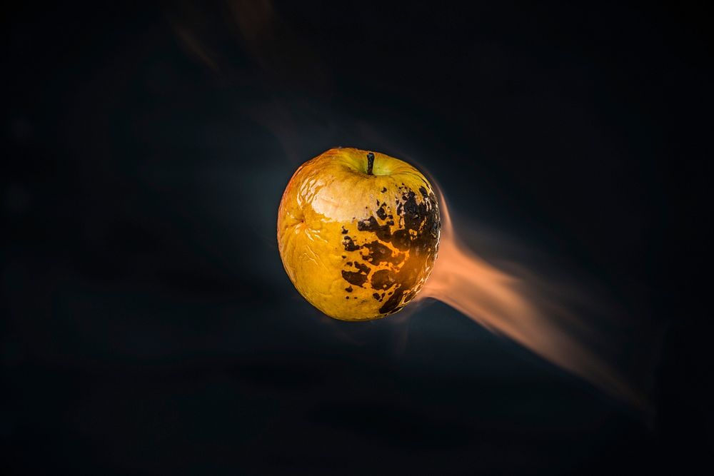 Apple charred and on fire on a black background. Original public domain image from Wikimedia Commons
