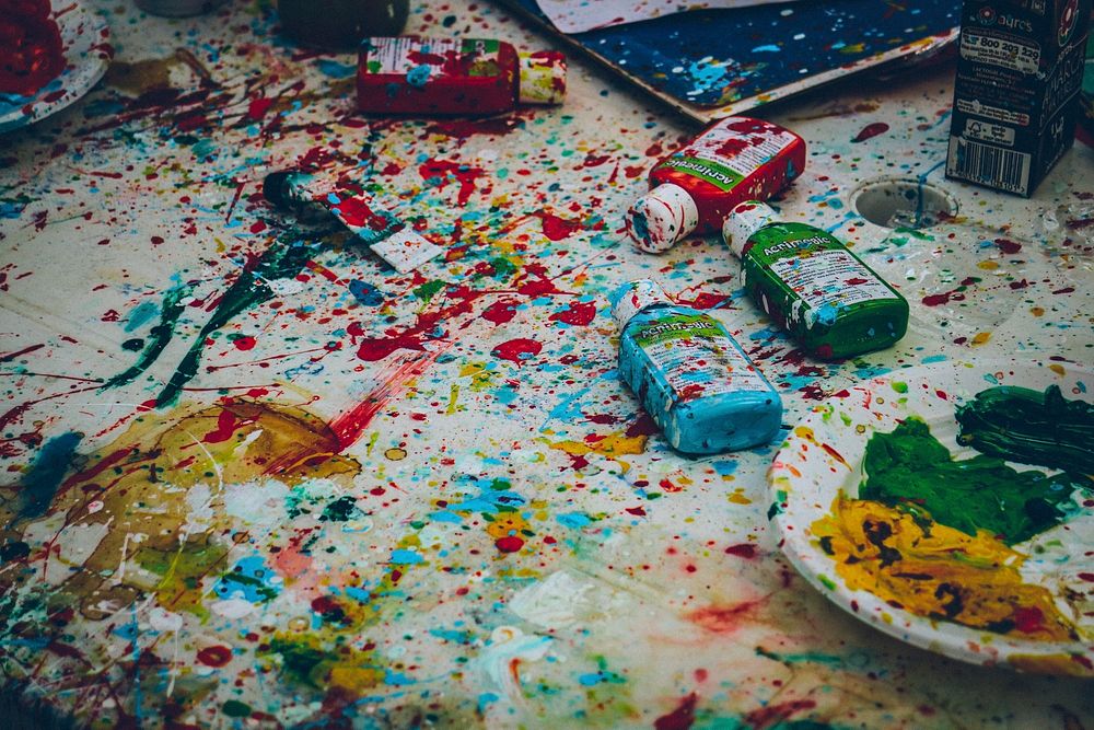 Splattered colorful paint over a white table with bottles of paint in Praia de Santa Cruz. Original public domain image from…