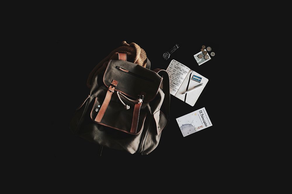 A backpack, a watch, a “Little Prince” book and coins against a black background. Original public domain image from…