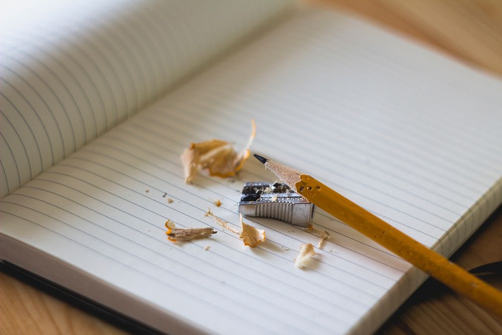 Pencil shavings around a pencil and a pencil sharpener on an open notebook. Original public domain image from Wikimedia…