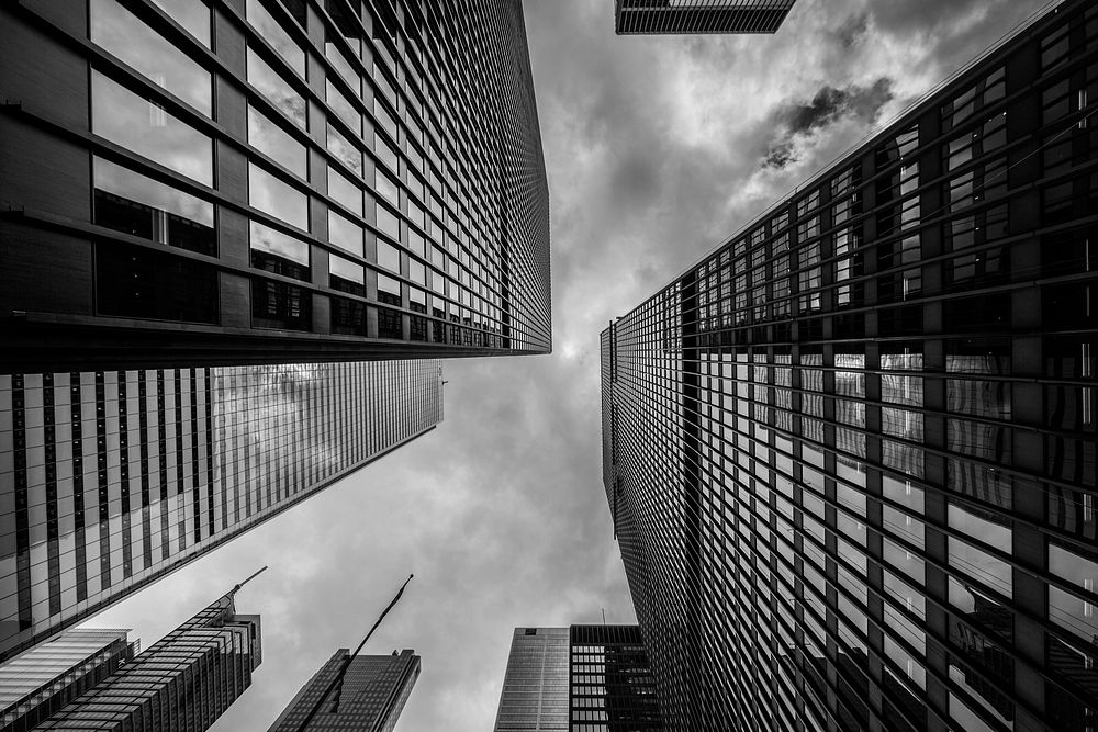 A black-and-white shot of white clouds above towering high-rises in a city. Original public domain image from Wikimedia…