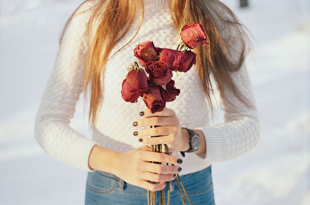 Low Shot of woman holding a bouquet of dried and wilted red roses. Original public domain image from Wikimedia Commons