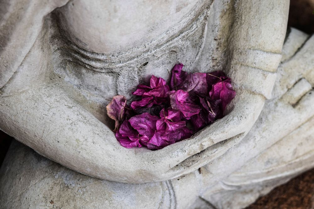 A bunch of purple flowers in the hands of a statue of a person sitting cross-legged. Original public domain image from…