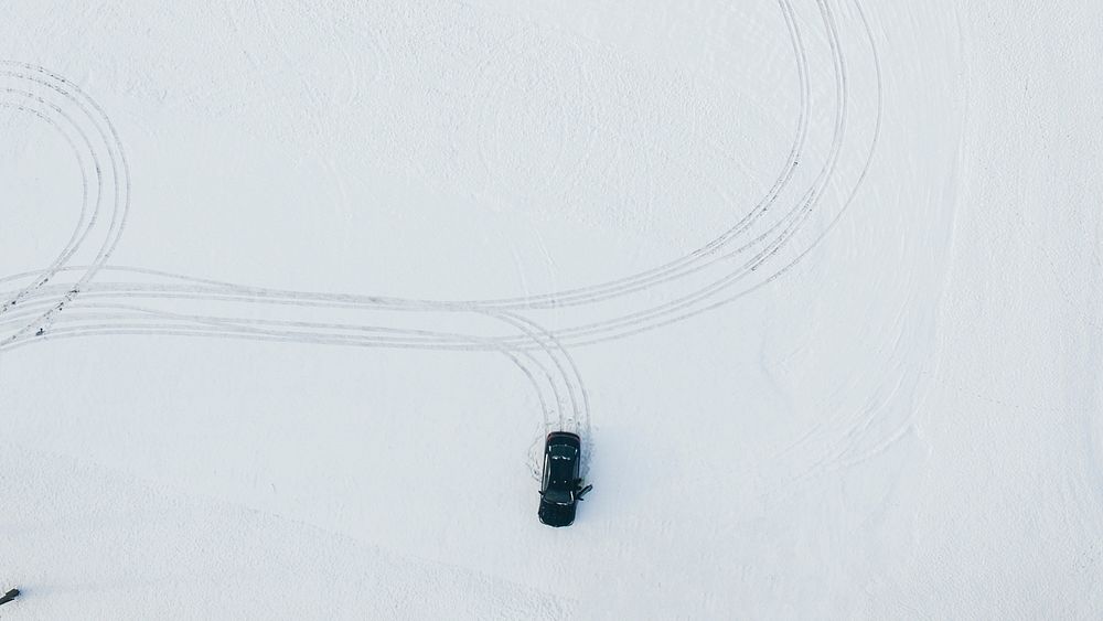 A drone shot of a car leaving tire marks in the snow. Original public domain image from Wikimedia Commons