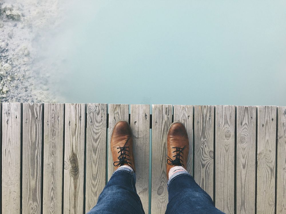 A person standing on a dock looking down on their brown shoes next to the water. Original public domain image from Wikimedia…