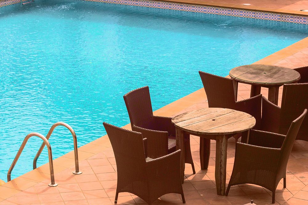 Rattan chairs around small wooden tables by a pool. Original public domain image from Wikimedia Commons