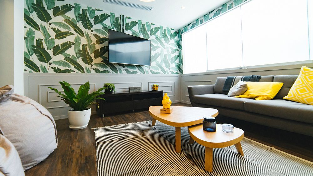 A room with palm print wallpaper, bean bag chairs, a couch, coffee table, rug, and tv at Communal Coworking. Original public…