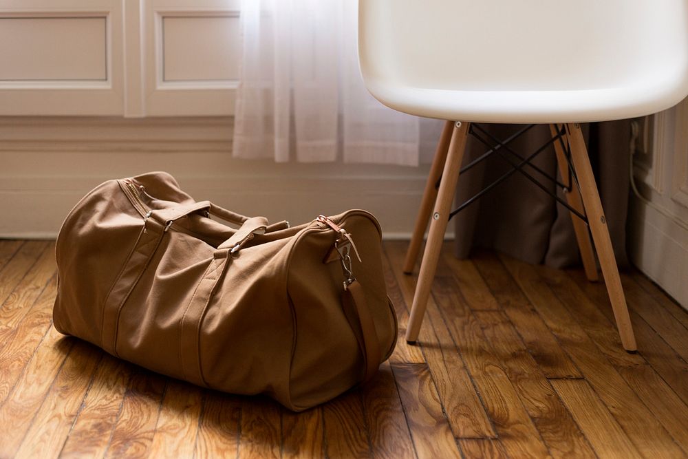 A leather duffel bag on the floor next to a small white chair. Original public domain image from Wikimedia Commons