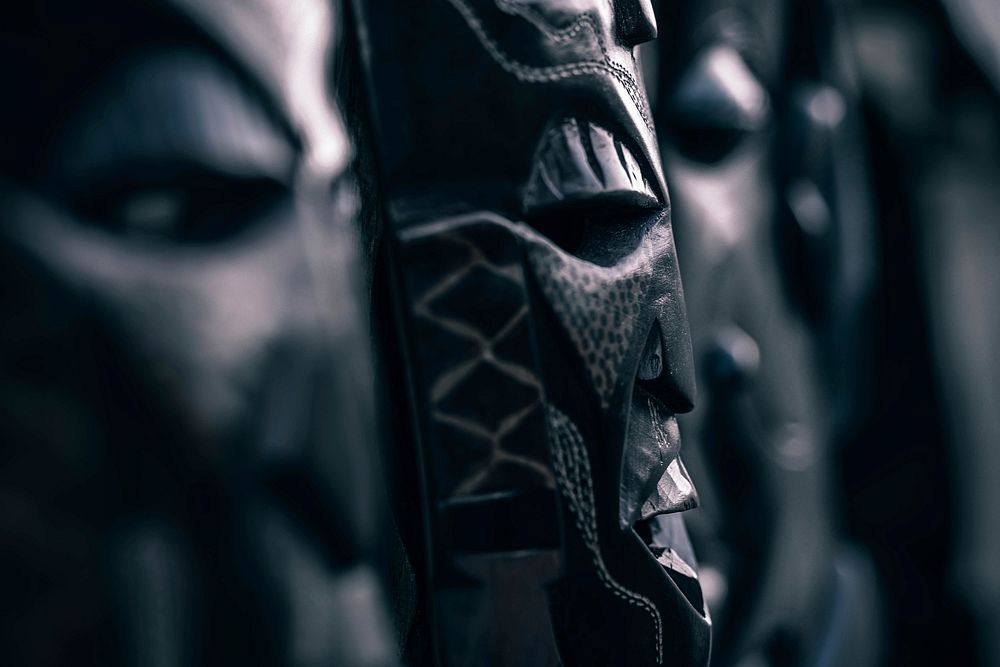 A dim close-up of wooden tribal masks. Original public domain image from Wikimedia Commons