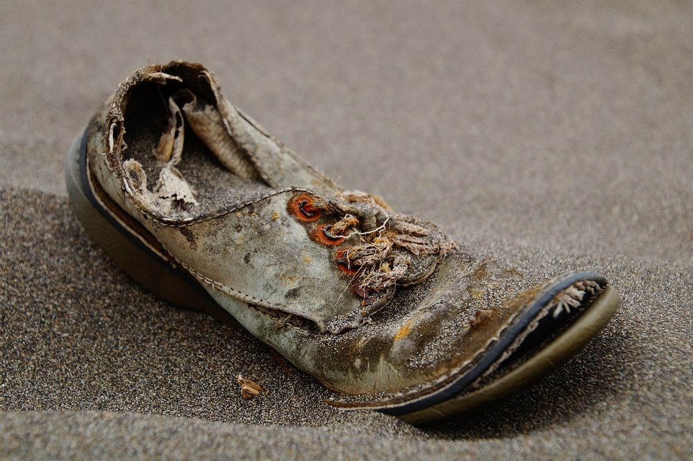An old pair of men's lace shoes sitting in the sand in Chile. Original public domain image from Wikimedia Commons