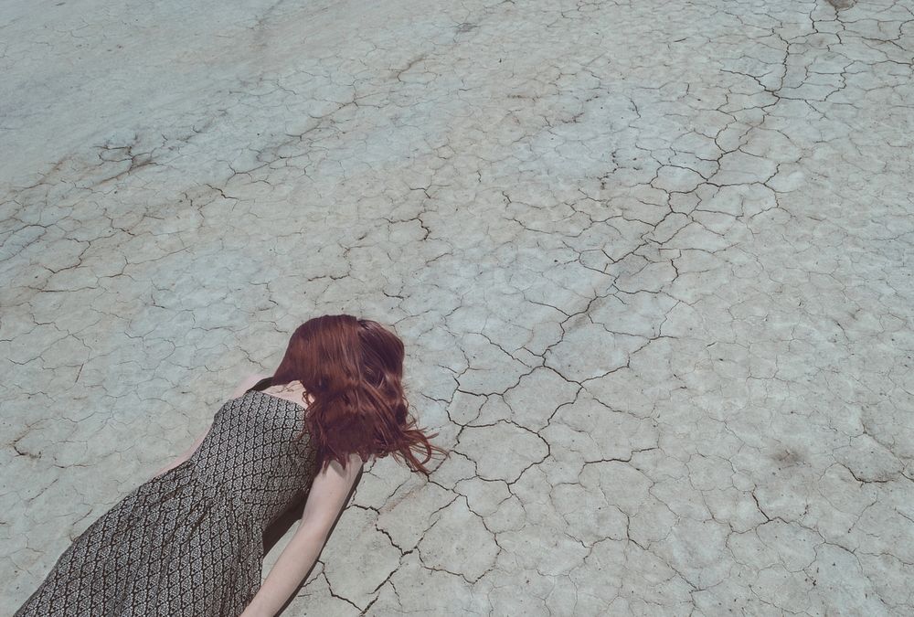 Woman with hair over face lying down on cracked desert floor. Original public domain image from Wikimedia Commons