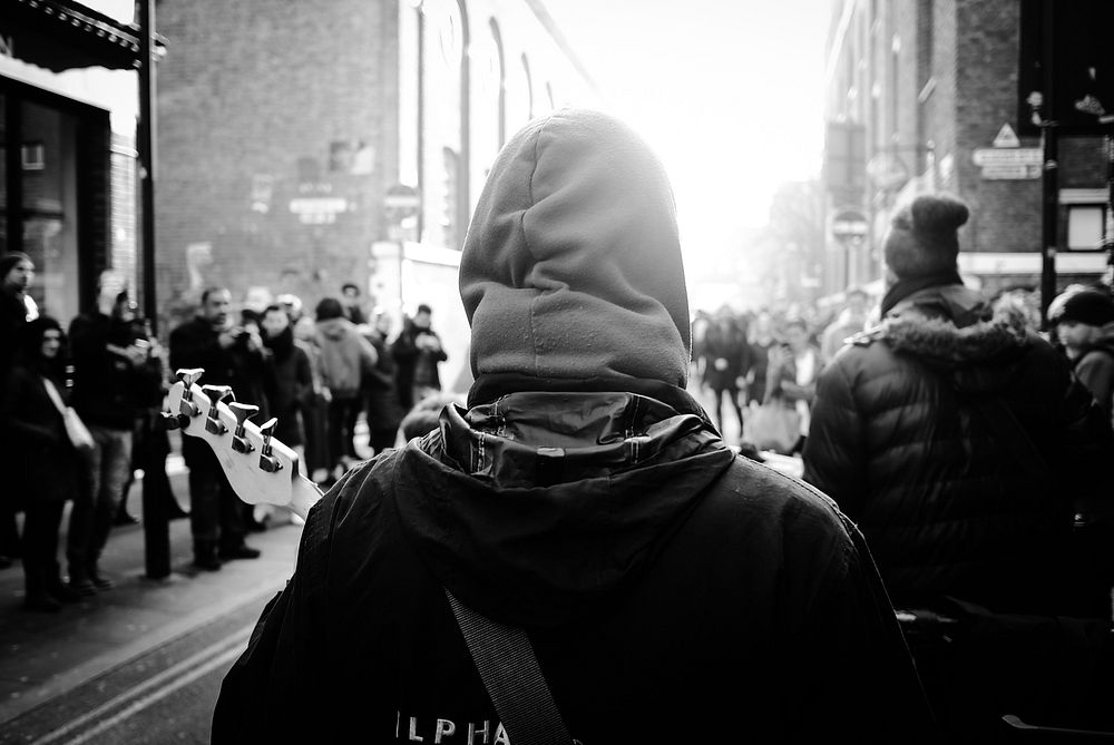 A black and white shot from behind civilians wearing hooded jackets and walking through London. Original public domain image…