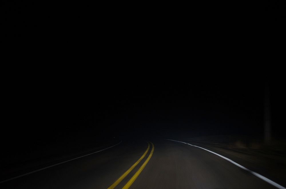 A dark night photograph from dash view of a car driving on a two-way road in Fenton. Original public domain image from…