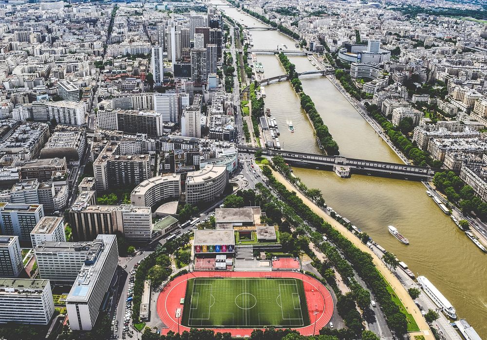 Drone shot of Paris showing skyscrapers, a soccer and track field, and boats on river Seine. Original public domain image…