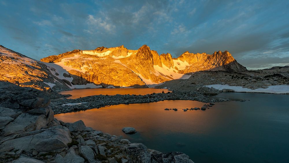 A snowcapped mountain range at Isolation Lake, with a sunset casting a bright light over the peaks. Original public domain…