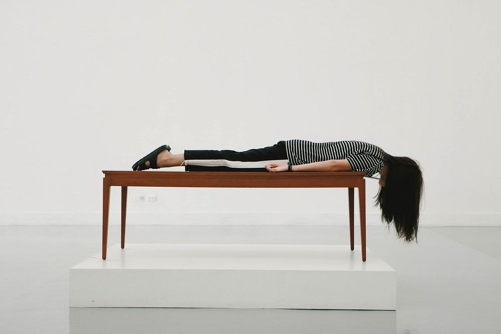 Lady at the Bangkok Art and Culture Centre lays on stomach on a wood table. Original public domain image from Wikimedia…