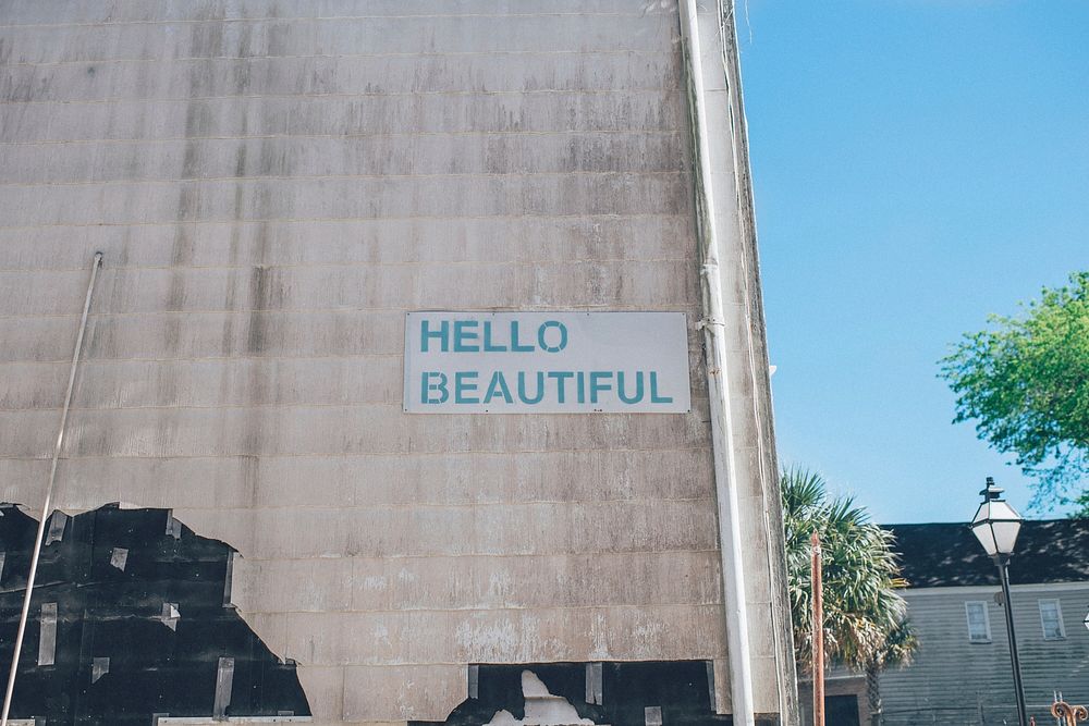 Green hello beautiful sign on urban wall with blue sky in background, Charleston. Original public domain image from…