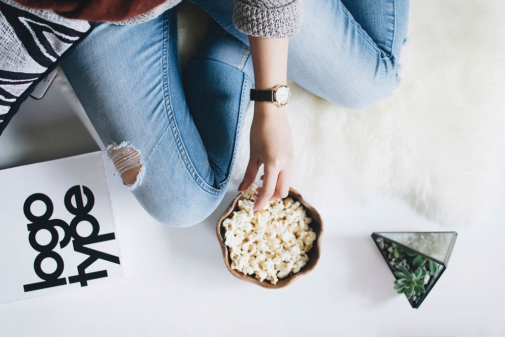A person in ripped jeans eating popcorn alongside a succulent plant and typographic sample. Original public domain image…