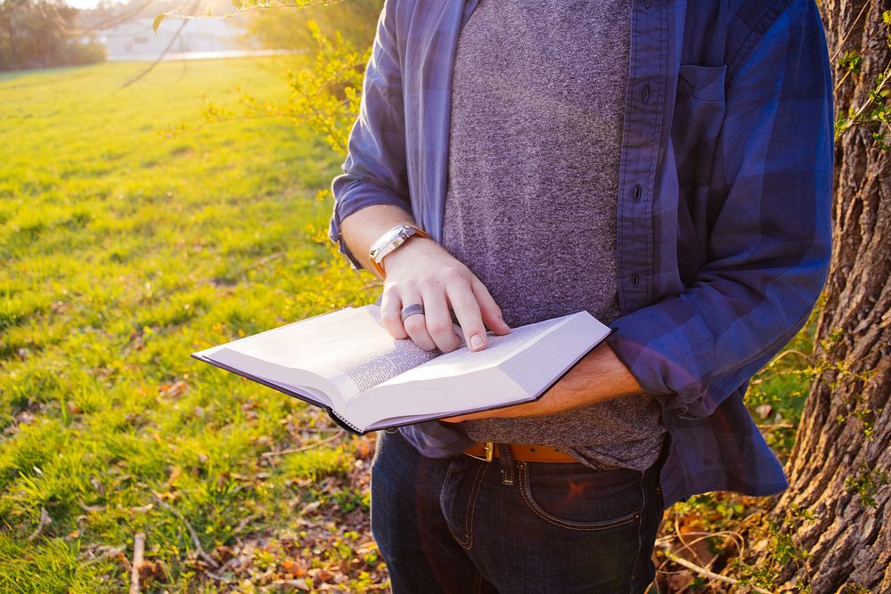 Man holding a book in outdoor area. Original public domain image from Wikimedia Commons