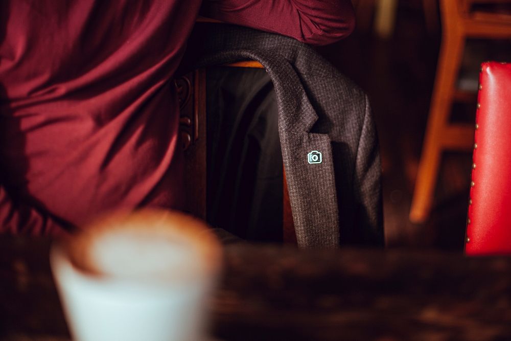 A blazer with an Unsplash pin, hanging on a chair at a cafe table. Original public domain image from Wikimedia Commons