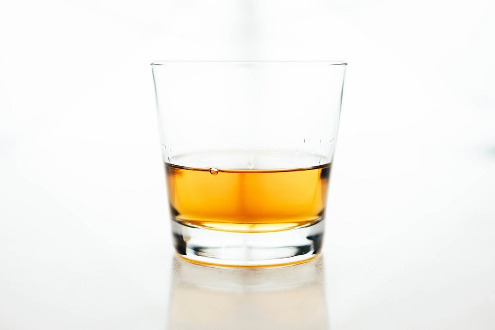 The macro view of a glass cup containing whiskey in a white background. Original public domain image from Wikimedia Commons