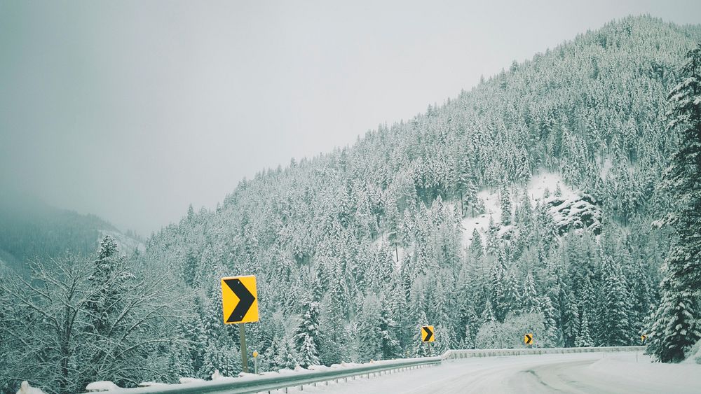 Yellow and black chevron signs on the side of a snowy road in the Rocky Mountains. Original public domain image from…
