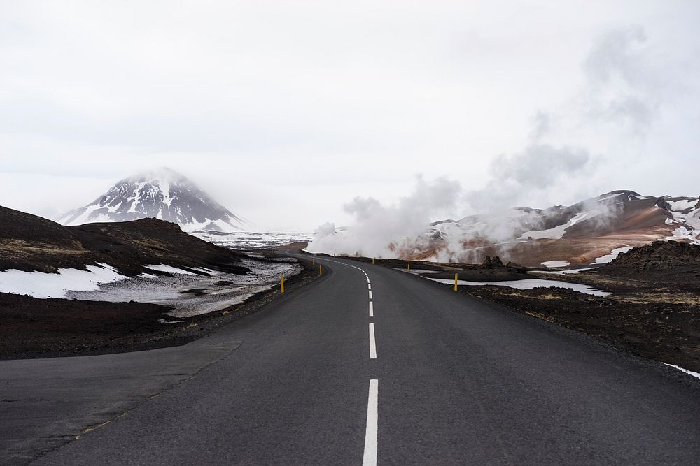 An asphalt road in the mountains with steam rising up on the roadside. Original public domain image from Wikimedia Commons