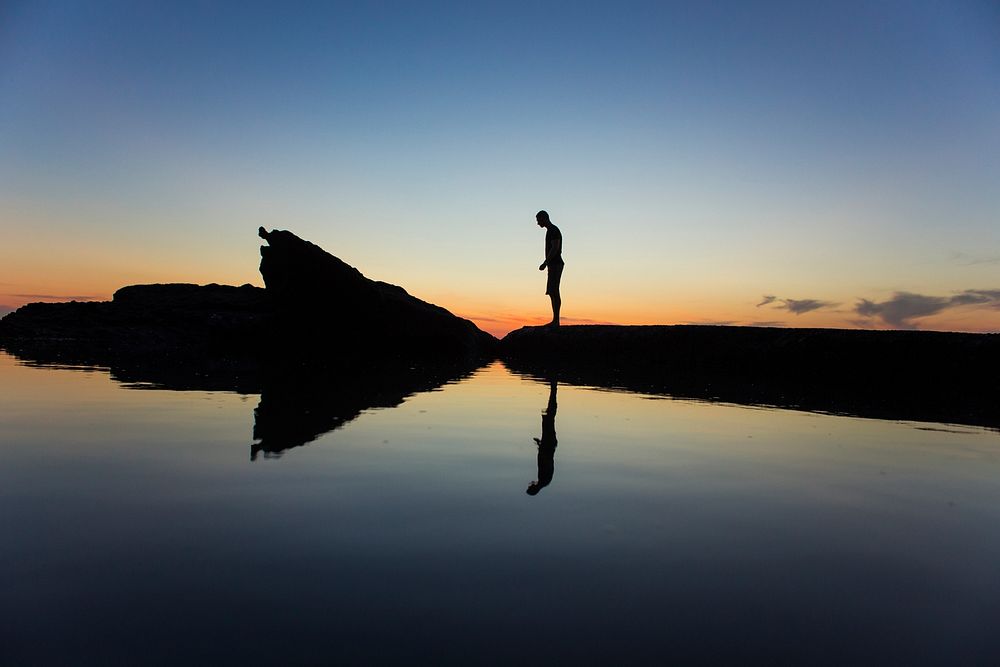 Man silhouette standing on the rock with reflection at Virginia Beach after sunset. Original public domain image from…