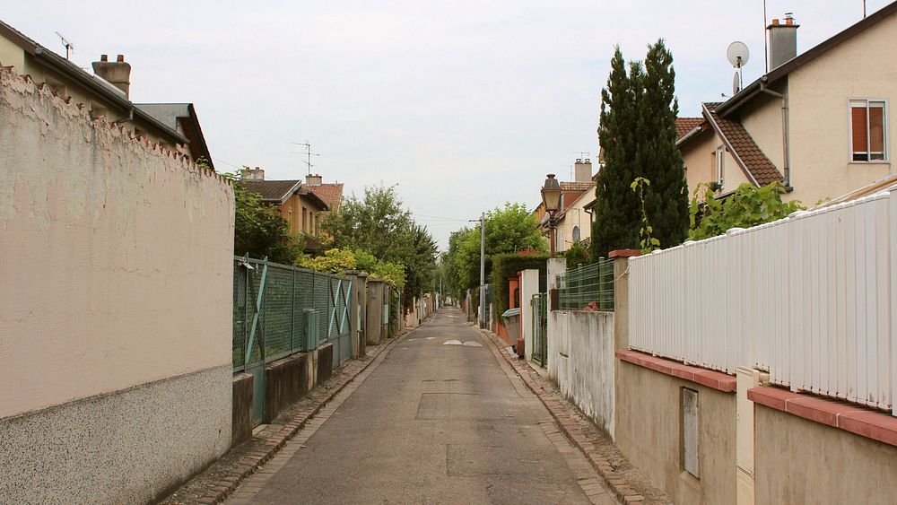 Street in an urban setting with fences surrounding houses along the road. Original public domain image from Wikimedia Commons