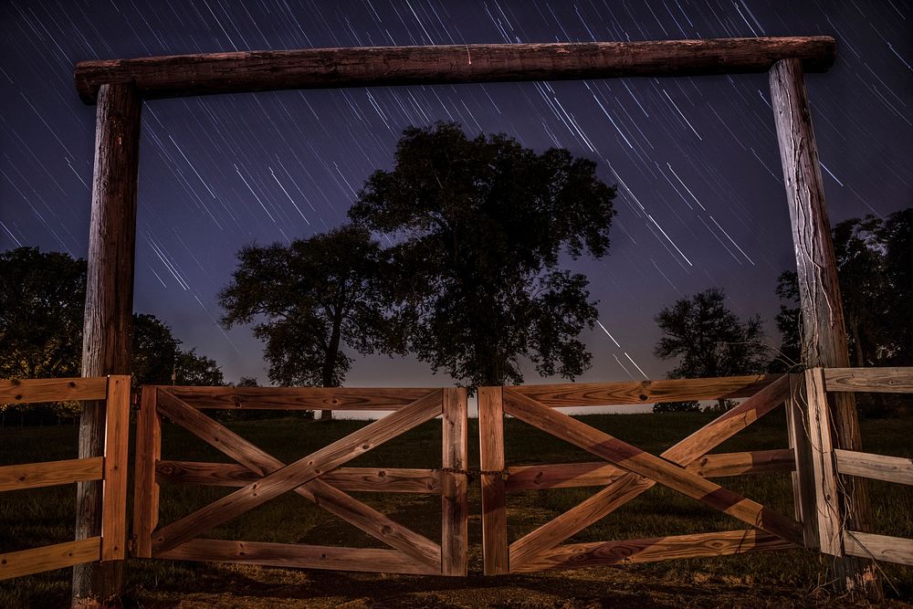 An archway with a gated fence in Lebanon, featuring blurry star trails in the background. Original public domain image from…