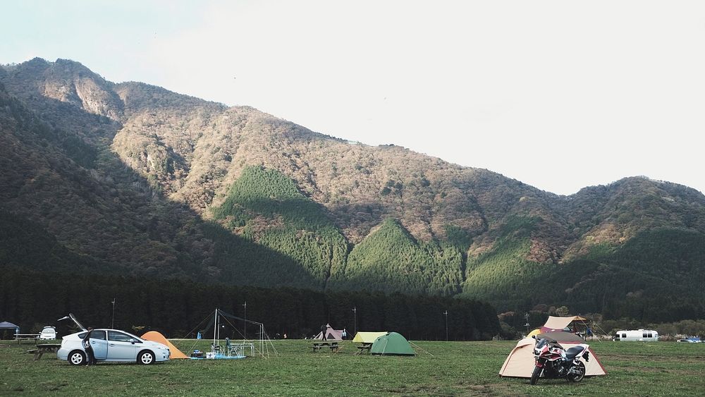 Campground with tents and cars in front of a forested mountain. Original public domain image from Wikimedia Commons