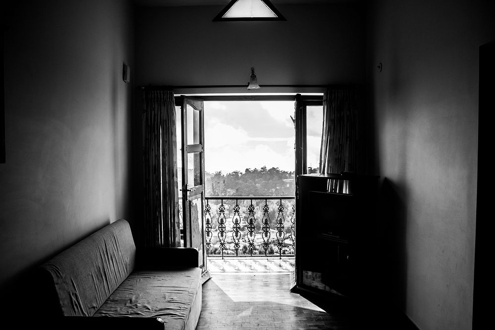 Black and white shot of worn down sofa and balcony window with view from flat, Kodaikanal. Original public domain image from…