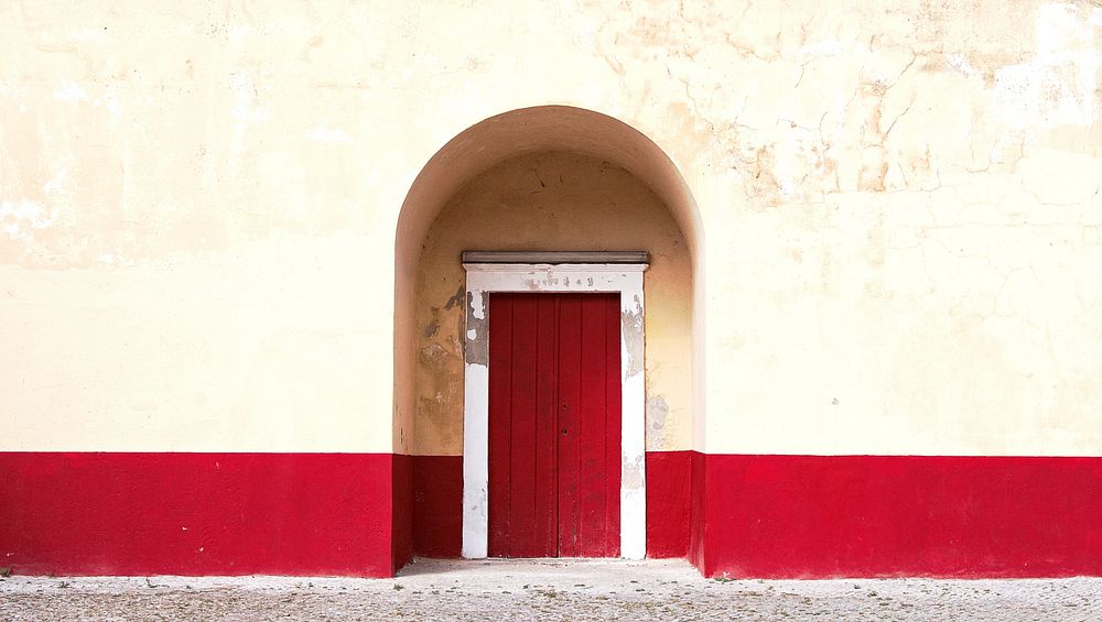 White and red arch door way with a stone walkway outside the door. Original public domain image from Wikimedia Commons