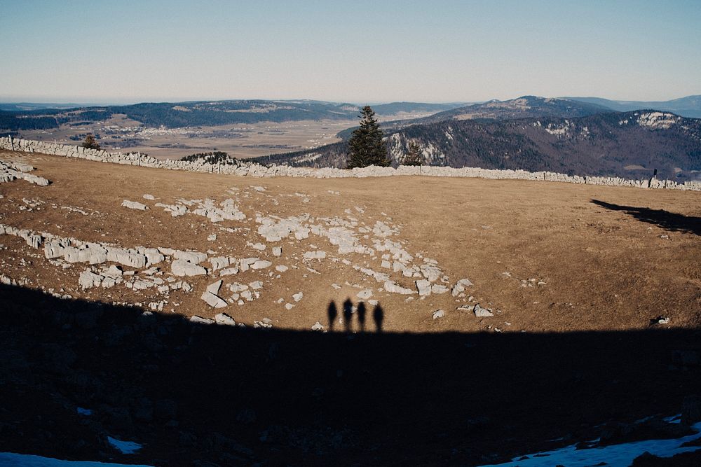 Shadows of four people standing on elevated terrain on a rocky plain the mountains. Original public domain image from…