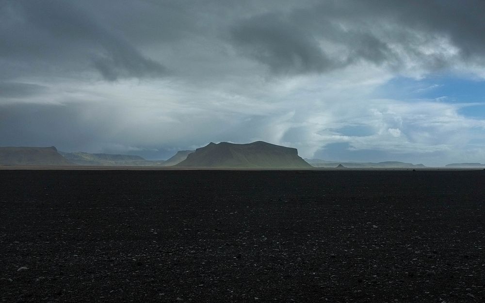 A rocky plain with flat mountains on the horizon on a cloudy day. Original public domain image from Wikimedia Commons