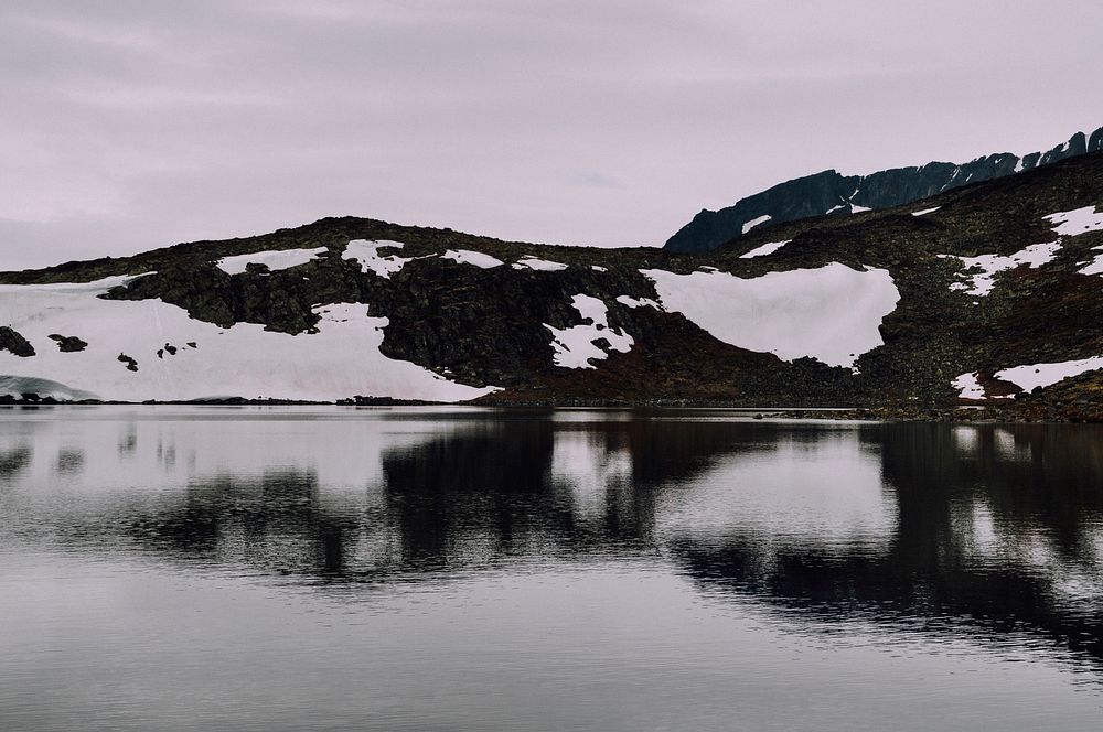 Snow on Besseggen mountain ridge in Norway reflects in a dark lake. Original public domain image from Wikimedia Commons